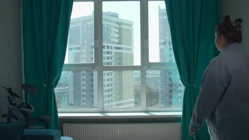 Junge Frau genießt morgens den Blick durch das Panoramafenster zu Hause.