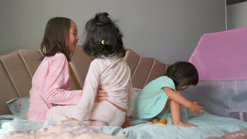 Three Happy Children Play on Bed in Pajamas