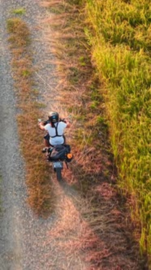 Aerial View of a Motorcyclist Exploring Rural Dirt Roads Between Green Fields
