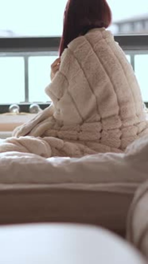 Woman Wrapped in Cozy Blanket Sits on Bed