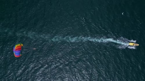 Drohnenvideo eines farbenfrohen Parasailers, der von einem Schnellboot über den Ozean gezogen wird. Die Szene fängt das ein