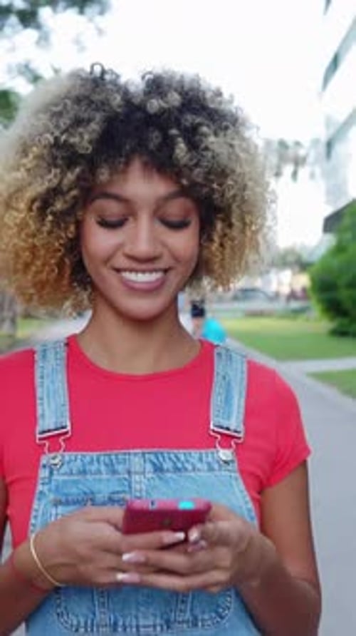 Smiling Woman Types on Phone in Urban Setting