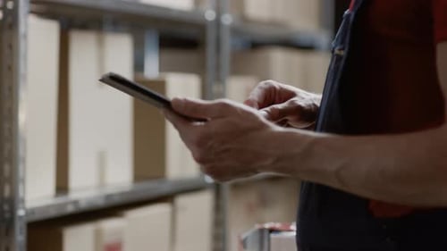 Gros plan sur les mains d'un homme utilisant une tablette numérique alors qu'il se tient debout dans l'entrepôt.