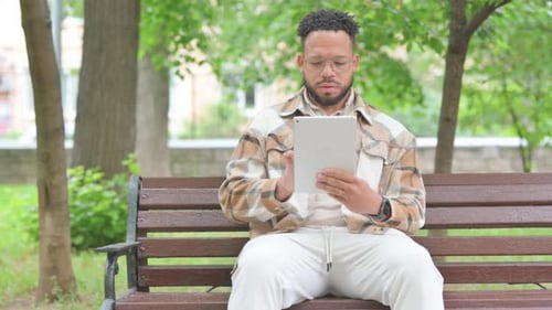 Young Multi Ethnic Man Using a Digital Tablet Outdoor on Bench