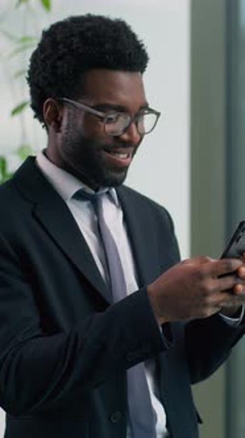 African American Businessman Smiling Looking at Smartphone in Modern Office Happy Male Professional