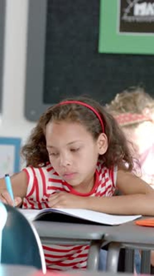 Vertical video: In school, girl smiling and writing in notebook during classroom activity