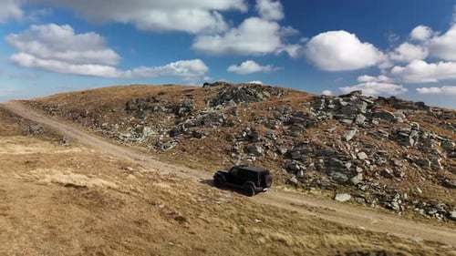Off-road vehicle drives through rugged hills on a clear day with a scenic sky