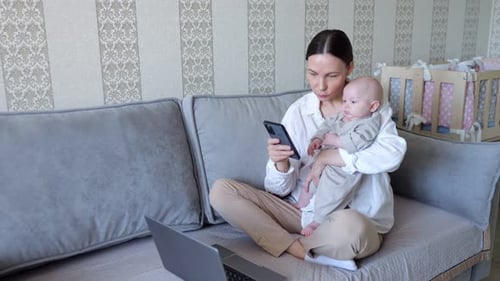 Woman with Baby Using Cellphone on Couch