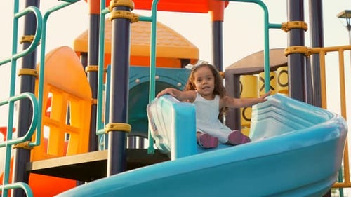 Latin beautiful little girl enjoying and playing in the park games on the slide sliding down