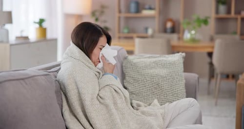 Woman Blowing Nose with Tissue Under Blanket