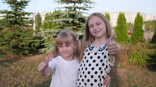 Two Cute Girls Giving Thumbs Up in Park
