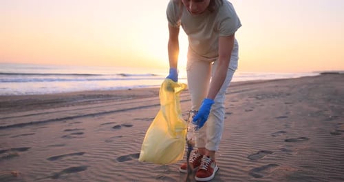 Una mujer ecológica recoge botellas de plástico en una playa durante las vacaciones de verano. Día de la Tierra. Cámara lenta