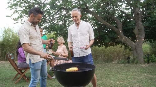 Buddy Male Friends Enjoying Outdoor Summer BBQ In Garden Toasting Beer While Cooking