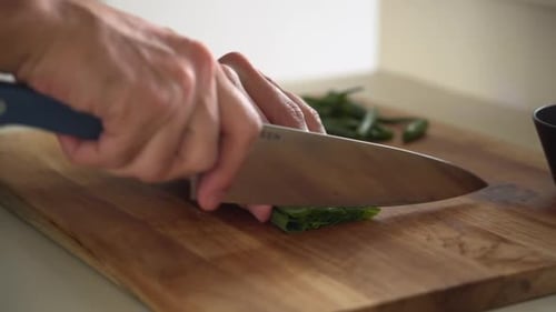 Professional chef chopping spring onions on a wooden cutting board, medium shot