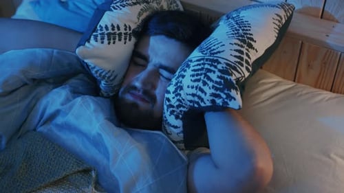 Un homme dort paisiblement dans sa chambre confortable entouré d'oreillers et de couvertures moelleux