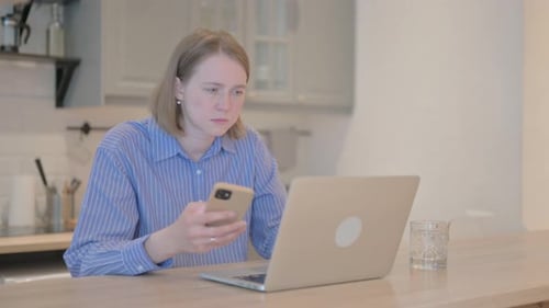 Young Adult Using Phone and Laptop at Table