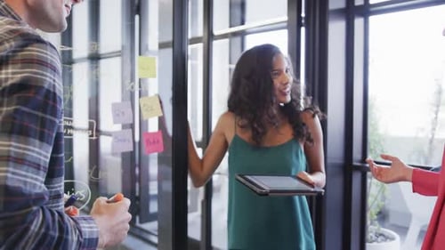 Diversos colegas criativos em discussão, fazendo anotações na parede de vidro no escritório, câmera lenta