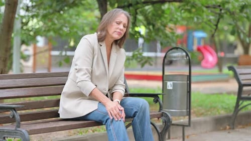 Woman Massages Knee on Park Bench Outdoors