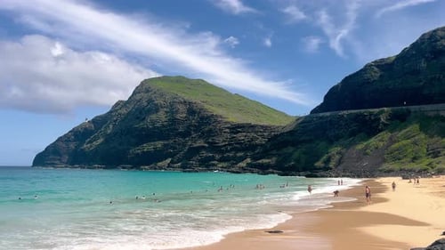 Une plage tropicale aux eaux turquoises entourée d'imposantes falaises verdoyantes et où les baigneurs se détendent