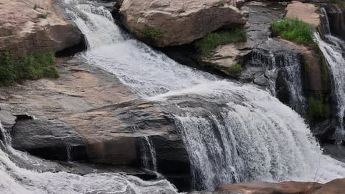 Tranquil Waterfall Flows Over Stones Surrounded By Lush Greenery Under Bright Sunlight