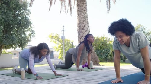 Instructor afroamericano que guía a las mujeres desde la postura de un niño hasta convertirse en cobra sobre colchonetas, alineando el cuello