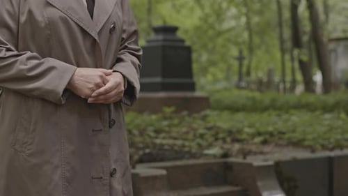 Unerkennbare Frau steht am Grab auf dem Friedhof