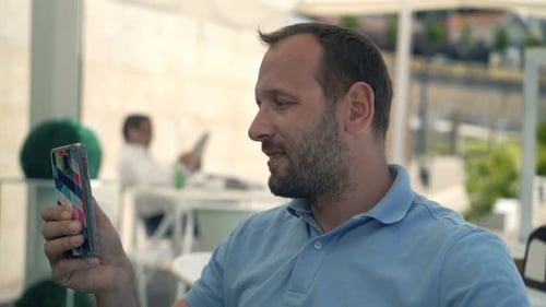 Jeune homme envoyant des SMS sur smartphone au café de la ville par une belle journée ensoleillée