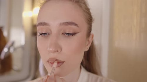 Gros plan du visage d'une jeune femme se maquillant en appliquant un crayon à lèvres nude sur ses lèvres en créant