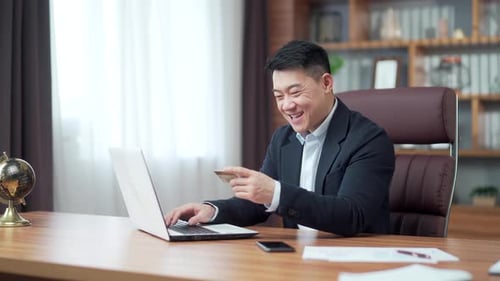 Happy asian business man shopping online customer paying by bank credit card sitting in a modern