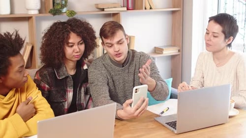 Young Man Demonstrating on the Smartphone the Concept of His Work Ideas to Multiracial Corporate