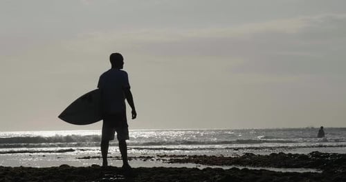 Silhouette bei Sonnenuntergang eines Surfers an der Küste mit Blick auf den Horizont, bevor er sich auf den Weg macht