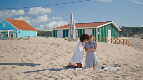 Lesbisches Paar überprüft Strandbilder mit dem Smartphone. Zwei Mädchen ruhen sich am Ufer aus und genießen