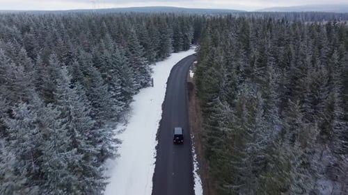Aerial Footage of Car Driving on a Curvy Road Through a Dense Snow Covered Pine Forest Wintry