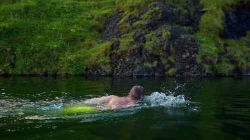 Tourist Swimming In The Seljavallalaug Pool With Moss-Covered Rocks At The Backdrop In Southern Regi