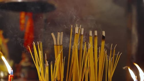 Close up of burning incense sticks releasing smoke in a traditional temple setting, creating a spiri