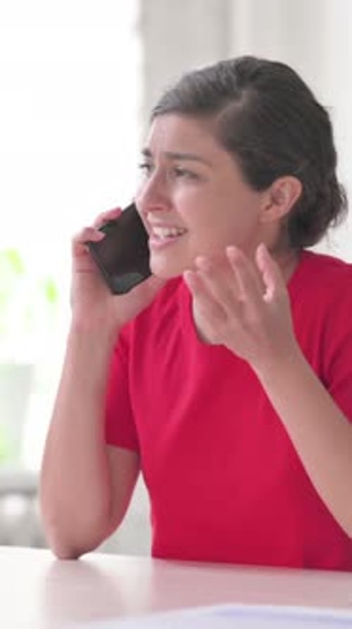 Frustrated Woman Talking on Phone Indoors at Table