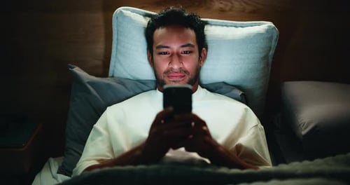 Man Relaxing in Bed Using Mobile Phone