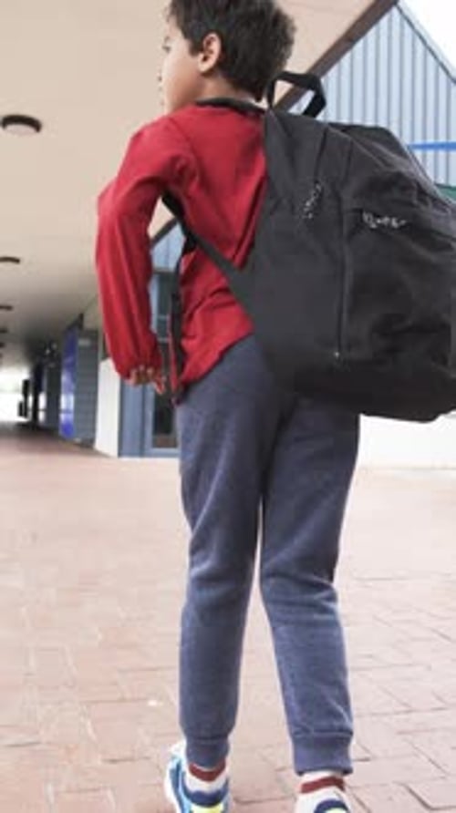 Vertical video: In school setting, young biracial student walks with black backpack