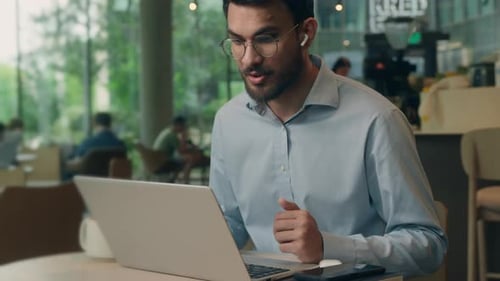 Young Man Video Conferencing on Laptop in Cafe