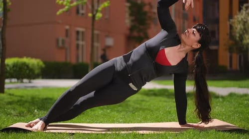 A Woman in a Sports Suit Performs the Pose of the Divine Sage Standing in a Side Plank with Palm and