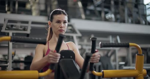 A Young Beautiful Brunette Girl in Sportswear is Exercising on a Machine in the Gym Doing Exercises