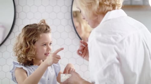 Woman Applying Cream to Child's Face in Bathroom
