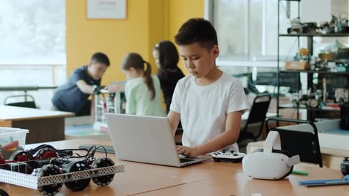 Konzentrierter Schüler, der in einer Klasse einer Robotikstunde an einem Laptop arbeitet und einen fahrenden Roboter programmiert
