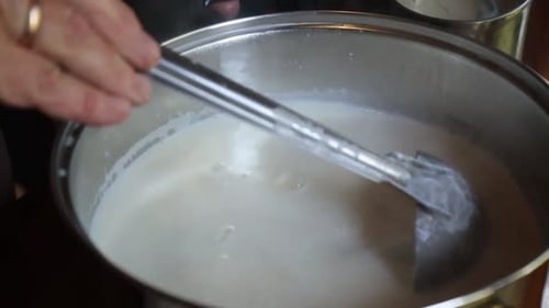 Person, die hausgemachten Käse zubereitet und geronnene Milch in einem Topf umrührt, während der Dampf aufsteigt, dabei ein warmes