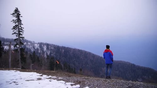 a Traveler in a Blue Jacket Looks at the Forest Winter and Mountains