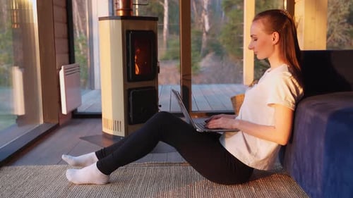 Woman Working on Laptop by Warm Fireplace at Home