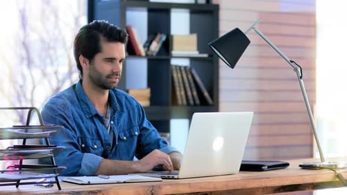 4K video footage of a young businessman working on a laptop while sitting at his desk in an office