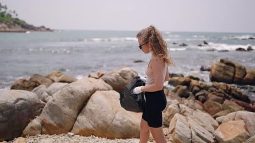 Woman Collects Plastic Trash on Rocky Shore Volunteers in Coastal Cleanup Mission to Tackle Marine