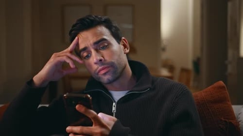 Frustrated Man Reading Message Smartphone in Dark Home Living Room Closeup
