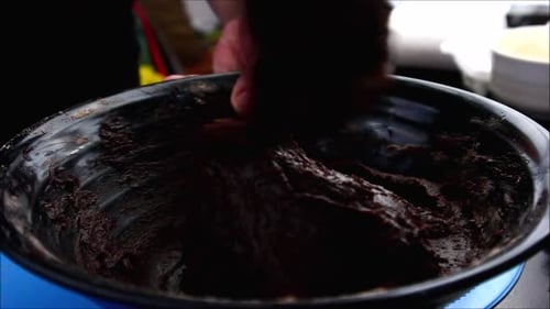 Handheld close up video shot of brownies batter in a bowl being mixed with a wooden spoon.